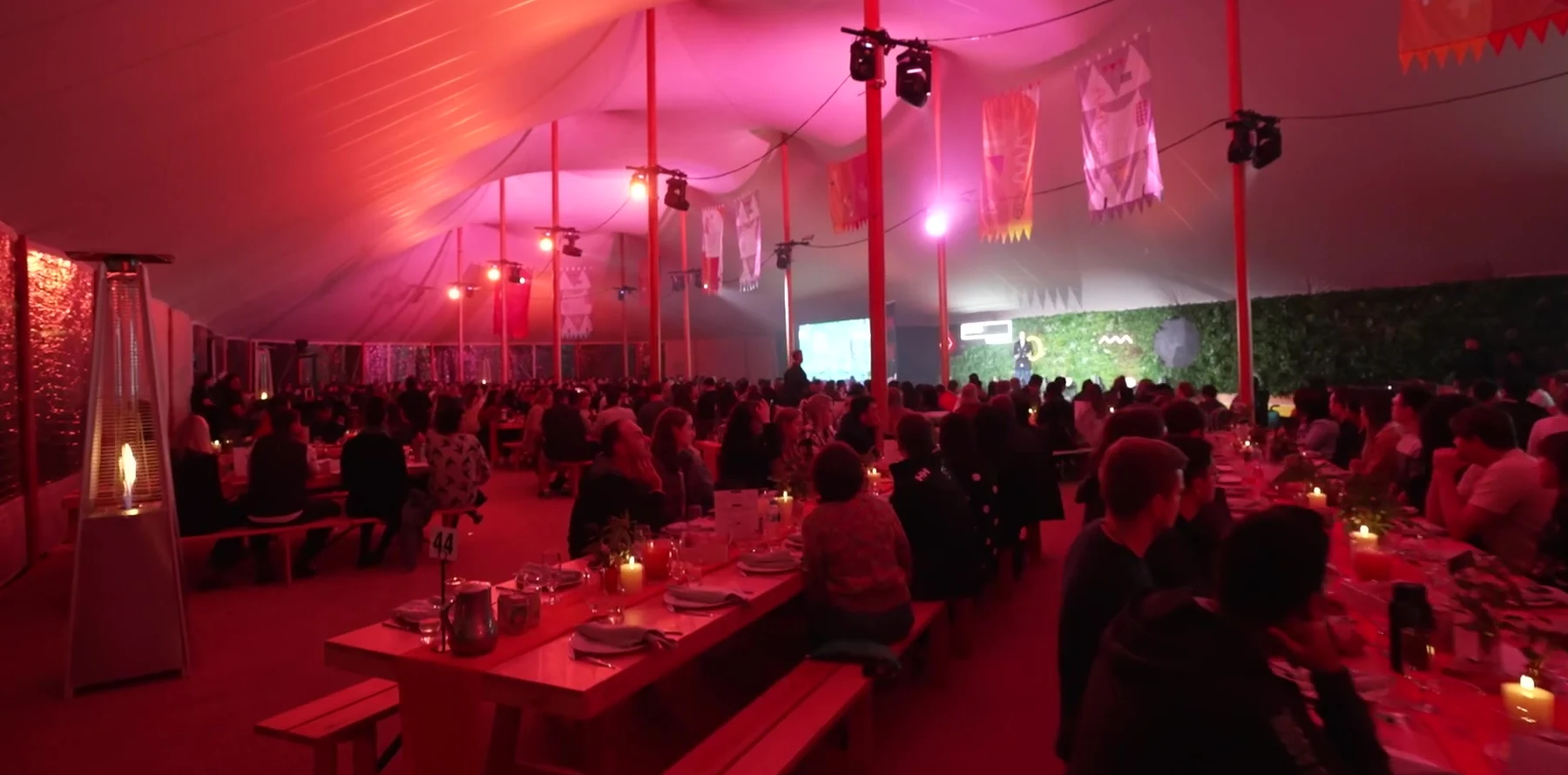 The main marquee at The Outside at night, long tables and a full room under red lighting