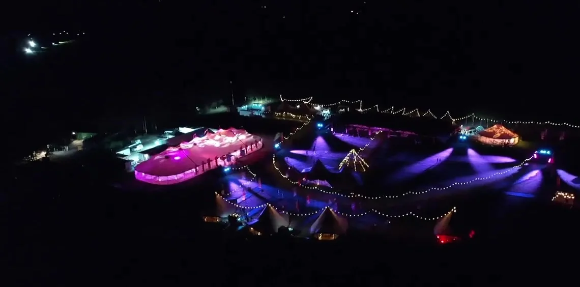 Aerial view of The Outside site lit up at night, marquees glowing against the dark valley
