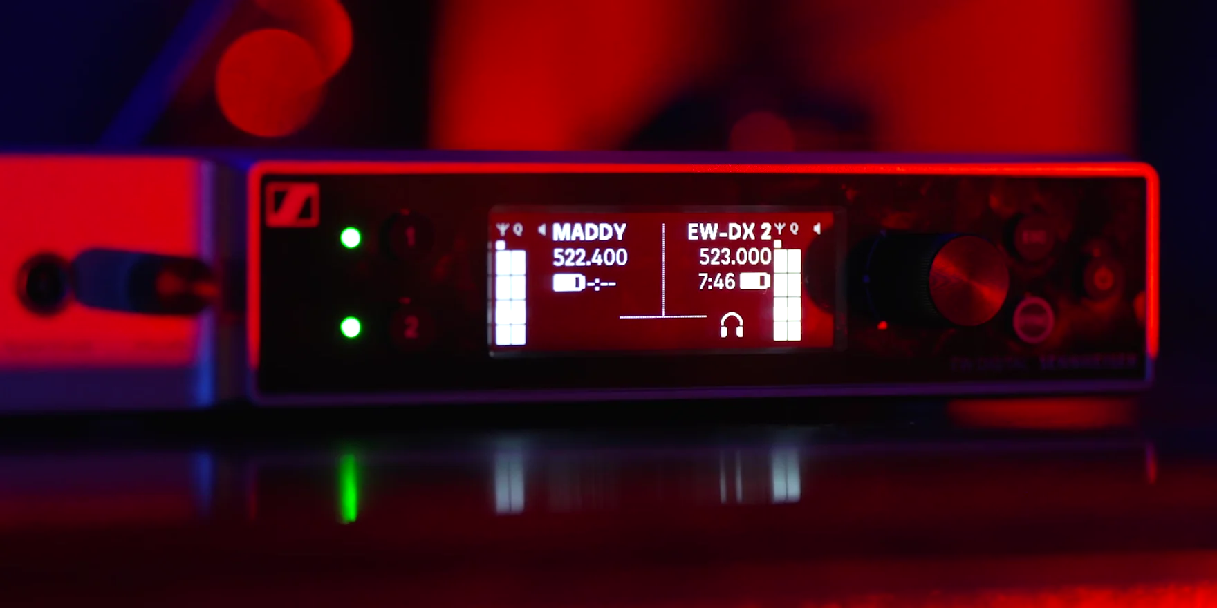 A Sennheiser EW-DX receiver on stage, its display reading MADDY, in red stage light