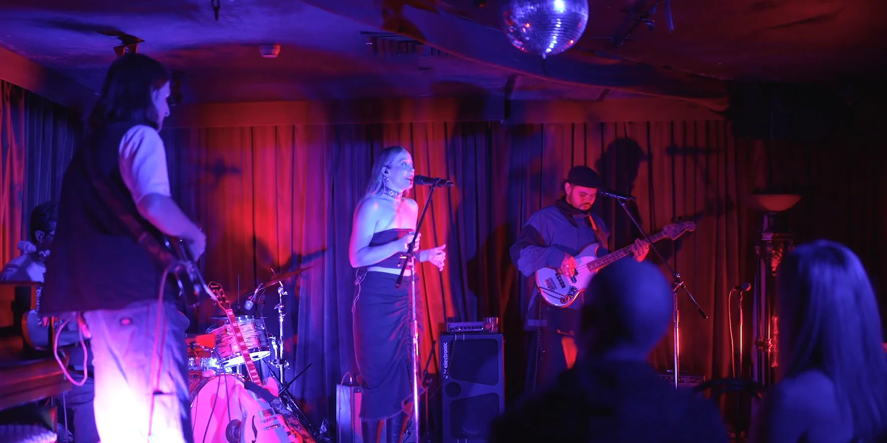Velvet Bloom playing live in a small red-lit room, the audience in the foreground